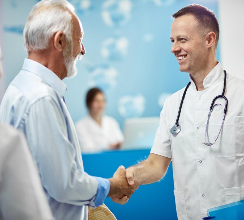 senior-man-his-doctor-shaking-hands-while-greeting-hallway-medical-clinic-focus-is-doctor senior-man-his-doctor-shaking-hands-while-greeting-hallway-medical-clinic-focus-is-doctor